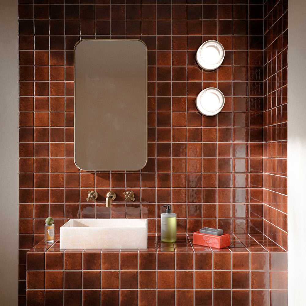 Bathroom featuring Levent Butterscotch Square 10x10cm gloss porcelain wall and floor tiles, showcasing rich caramel brown tones with subtle shade variation, paired with a stone basin, brushed brass taps, an arched mirror and contemporary wall lights.