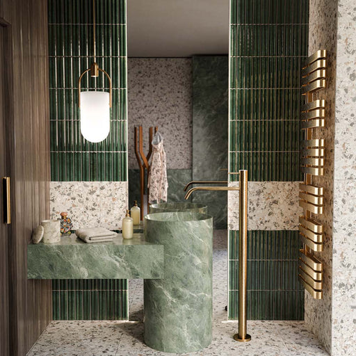 Bathroom featuring Levent Green Fluted Decor 6x24cm gloss porcelain wall tiles, showcasing deep green fluted detailing paired with terrazzo effect wall and floor tiles, green marble effect basins, brushed brass fittings and warm wood finishes for a luxurious contemporary space.