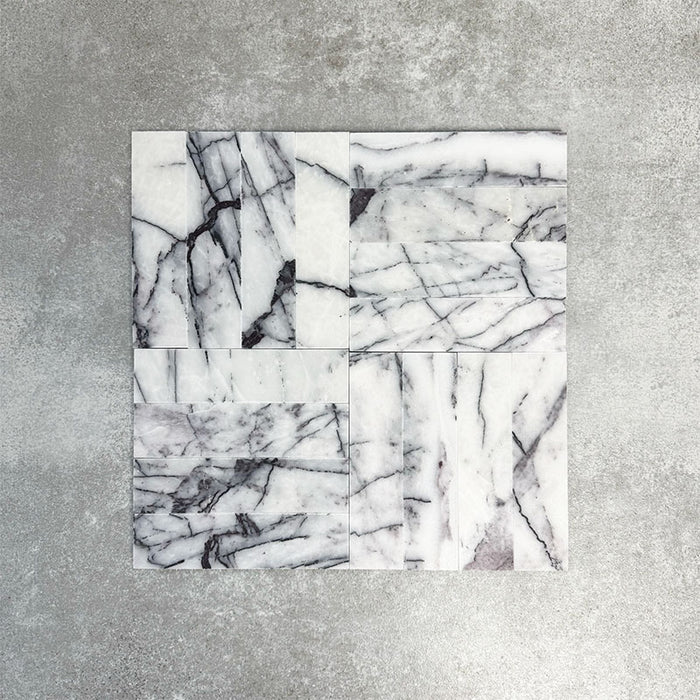 Arrangement of Fayrouz Lilac 5x20cm natural marble tiles with a honed finish, displayed in a mixed layout pattern to showcase variation, featuring a soft white base with flowing lilac and grey veining, highlighting the natural movement and individuality of each tile.