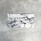Arrangement of Fayrouz Lilac 5x20cm natural marble tiles with a honed finish, displayed in a horizontal layout, featuring a soft white base with flowing lilac and grey veining, showcasing natural variation and the unique character of each tile.