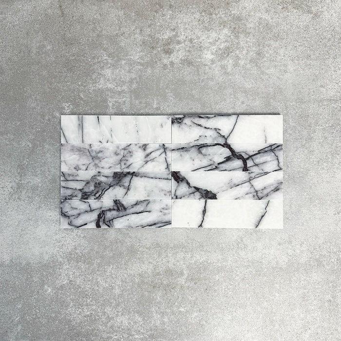 Arrangement of Fayrouz Lilac 5x20cm natural marble tiles with a honed finish, displayed in a horizontal layout, featuring a soft white base with flowing lilac and grey veining, showcasing natural variation and the unique character of each tile.