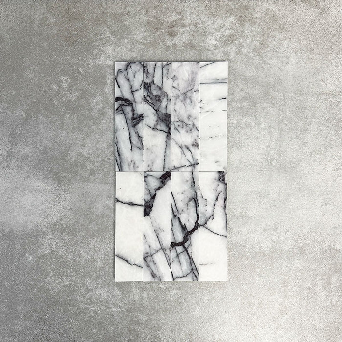Arrangement of Fayrouz Lilac 5x20cm natural marble tiles with a honed finish, displayed in a vertical layout to highlight variation, featuring a soft white base with striking lilac and grey veining, showcasing the natural movement and unique character of each piece.