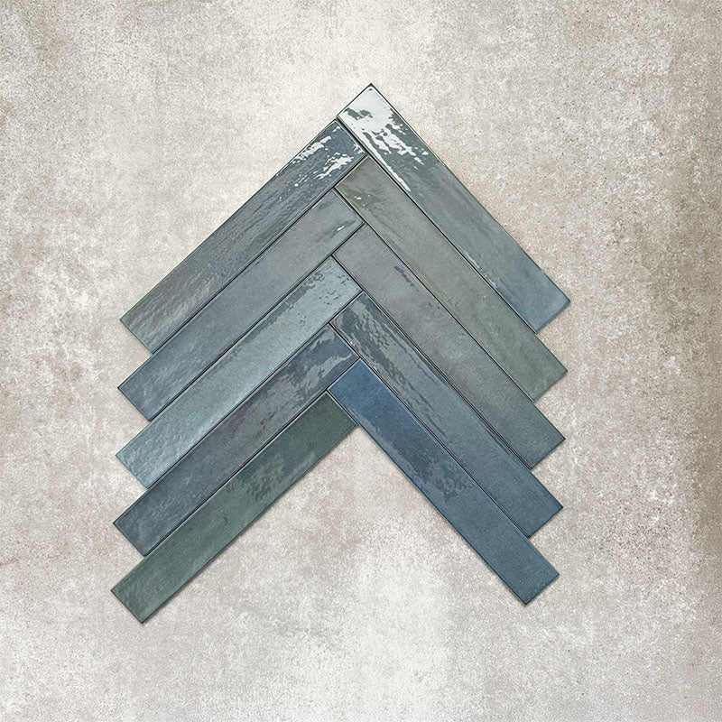 Close-up of Lisbon Blue 5cm x 30cm artisanal porcelain wall tiles arranged in a herringbone pattern, showcasing rich blue-grey tones, subtle tonal variation and a handcrafted-effect surface finish.