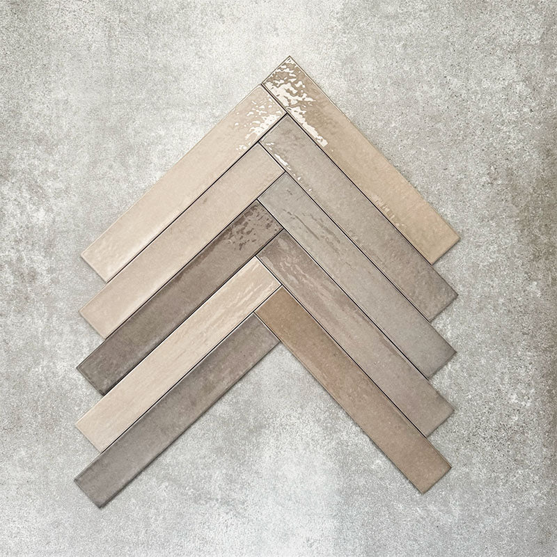 Close-up of Lisbon Grey 5cm x 30cm artisanal porcelain wall tiles arranged in a herringbone pattern, showcasing warm grey and taupe tones, tonal variation and a handcrafted-effect surface finish.