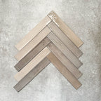 Close-up of Lisbon Grey 5cm x 30cm artisanal porcelain wall tiles arranged in a herringbone pattern, showcasing warm grey and taupe tones, tonal variation and a handcrafted-effect surface finish.