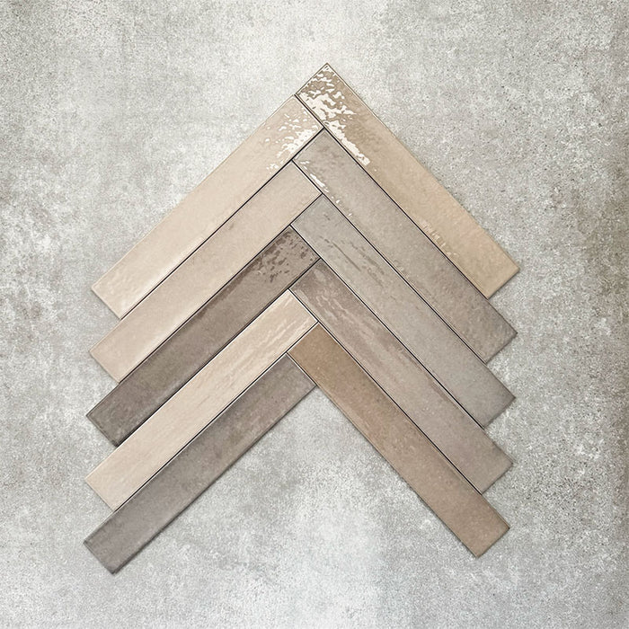 Close-up of Lisbon Grey 5cm x 30cm artisanal porcelain wall tiles arranged in a herringbone pattern, showcasing warm grey and taupe tones, tonal variation and a handcrafted-effect surface finish.