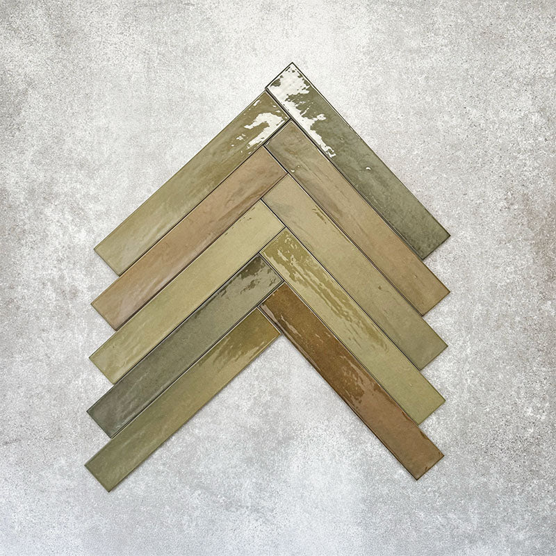 Close-up of Lisbon Olive Green 5cm x 30cm artisanal porcelain wall tiles arranged in a herringbone pattern, showcasing earthy olive green tones, tonal variation and a glossy handcrafted-effect surface finish.
