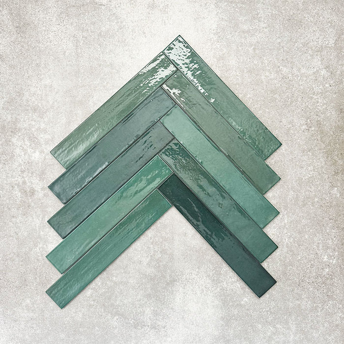 Close-up of Lisbon Verde Green 5cm x 30cm artisanal porcelain wall tiles arranged in a herringbone pattern, showcasing rich green tones, subtle tonal variation and a handcrafted-effect surface finish.