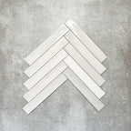 Close-up of Lisbon White 5cm x 30cm artisanal porcelain wall tiles arranged in a herringbone pattern, showcasing soft white tones, subtle surface variation and a handcrafted-effect finish.