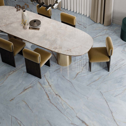Dining area featuring Lucca River Blue Lux 3D 60 × 120cm porcelain wall and floor tiles, styled with soft blue marble-effect tones, warm veining, velvet dining chairs, and contemporary neutral interiors.