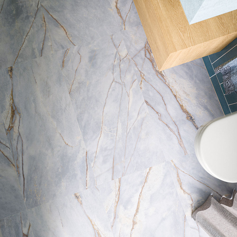 Lucca River Blue 60cm x 120cm matt tiles, showcasing soft blue-grey tones with flowing marble effect veining and warm golden detailing across a large-format bathroom floor.
