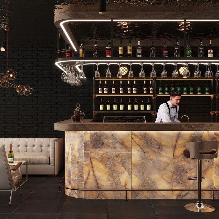 Contemporary bar interior featuring Lumen Precious Stone Amber 60 × 120cm polished porcelain tiles, showcasing rich amber, caramel, and smoky stone-inspired tones with layered crystalline detailing, dramatic mineral movement, and a reflective high-gloss finish, used across the illuminated bar frontage alongside dark interiors, warm metallic accents, and ambient feature lighting.