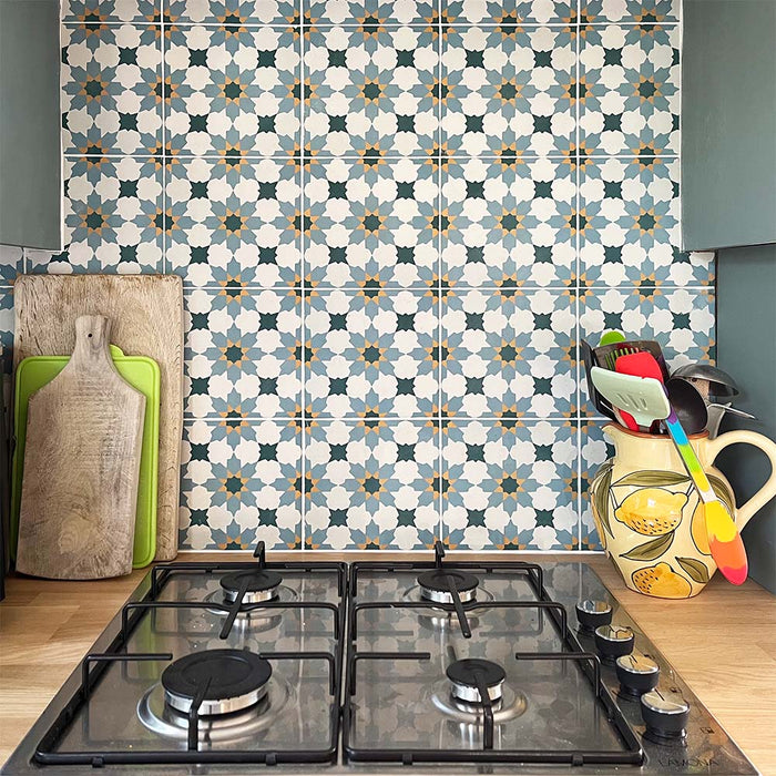 Madeira Anza 20cm x 20cm Moroccan style wall and floor tiles, featuring an intricate geometric pattern in blue, yellow and white, creating a colourful kitchen splashback paired with muted blue cabinetry and warm wooden worktops.