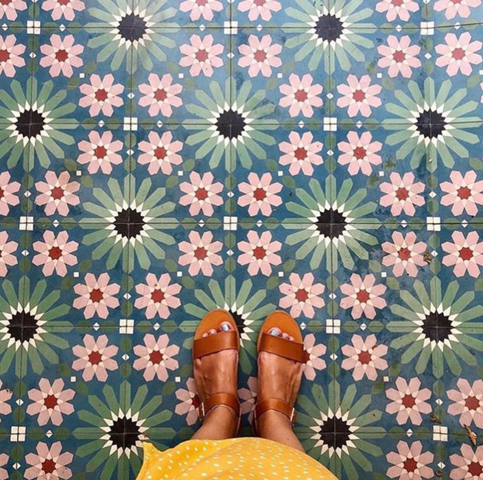 Floor featuring Fez Autumn 20x20cm Moroccan-style porcelain tiles, showcasing a rich geometric star pattern in earthy green, blue and blush pink tones, styled with tan leather sandals for a warm, bohemian look.