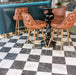 Interior setting featuring Fayrouz White 15.2x15.2cm natural marble tiles with a honed finish, installed in a classic chequerboard floor with black marble, styled with tan leather bar stools and a dark statement table.