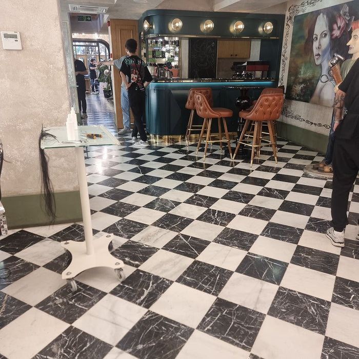 Interior setting featuring Fayrouz White 15.2x15.2cm natural marble tiles with a honed finish, installed in a classic chequerboard floor with black marble, styled with tan leather bar stools and a dark statement table.