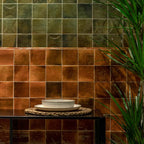 Interior detail featuring Saigon Amber Square Wall tiles in a Moroccan-inspired style, 10 × 10cm glossy ceramic tiles in warm amber tones, styled with layered tiles, greenery, and decorative tableware.