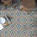 Living space featuring Balthazar Grand 20×20cm Moroccan-style porcelain floor tiles, showcasing an intricate geometric pattern in blue, brown and cream tones, styled with rustic wooden stools and warm natural textures for a bold, characterful finish.