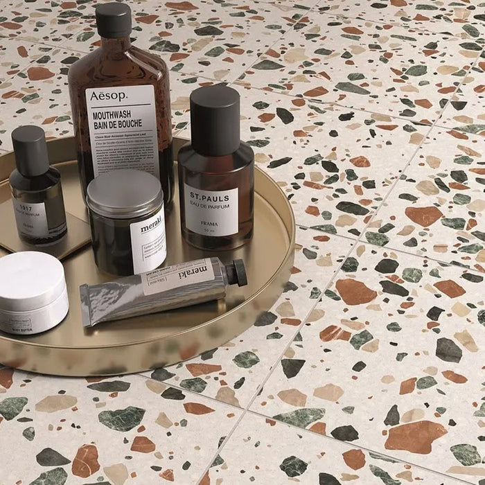 Close-up of Turin Terrazzo Blanco Drops porcelain floor tiles in a 20 × 20cm format, featuring a terrazzo-style design with larger scattered stone fragments in warm neutral tones, styled with bathroom accessories to highlight the texture and contemporary finish.