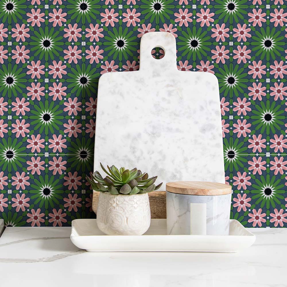 Fez Mini Autumn Moroccan-style porcelain tiles installed as a splashback, featuring a repeating geometric pattern in deep green, blush pink and charcoal tones. Styled with a white marble chopping board, small potted succulent and minimal accessories, highlighting the intricate 15 × 15cm pattern and its decorative, artisanal feel in a kitchen or utility setting.