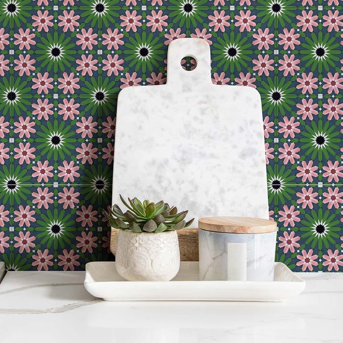 Fez Mini Autumn Moroccan-style porcelain tiles installed as a splashback, featuring a repeating geometric pattern in deep green, blush pink and charcoal tones. Styled with a white marble chopping board, small potted succulent and minimal accessories, highlighting the intricate 15 × 15cm pattern and its decorative, artisanal feel in a kitchen or utility setting.