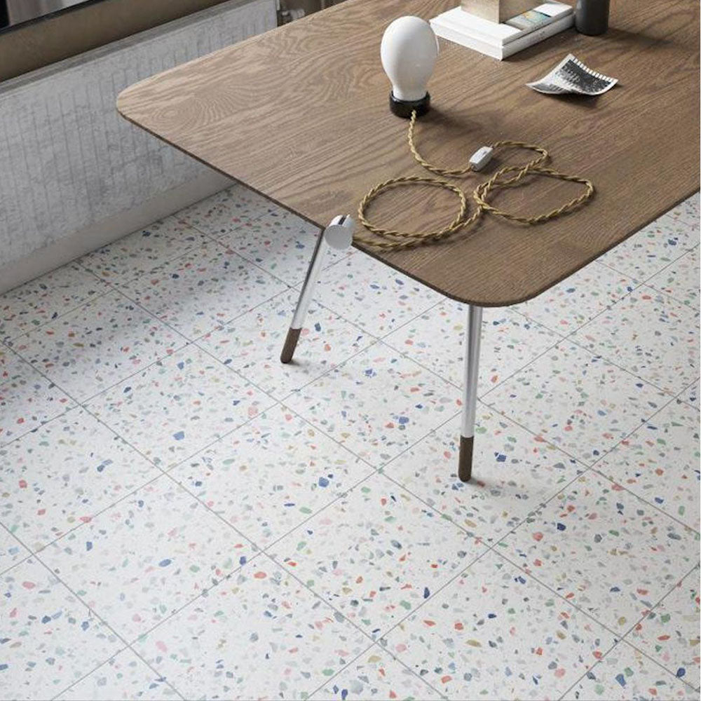 Interior floor featuring Gelato Tutti Frutti 25x25cm terrazzo-style porcelain tiles, showcasing a soft white base with multicoloured terrazzo flecks and styled with a wooden desk and modern accessories for a playful yet contemporary look.