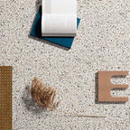 Close-up of Turin Terrazzo Blanco Dots porcelain tiles in a 20 × 20cm format, featuring a light terrazzo-style surface with subtle multicoloured stone fragments, styled with books and natural decorative objects to highlight the soft, contemporary finish.