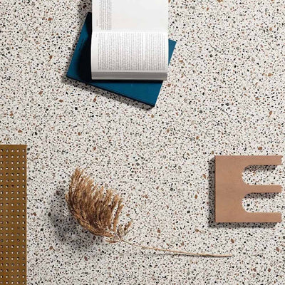 Close-up of Turin Terrazzo Blanco Dots porcelain tiles in a 20 × 20cm format, featuring a light terrazzo-style surface with subtle multicoloured stone fragments, styled with books and natural decorative objects to highlight the soft, contemporary finish.