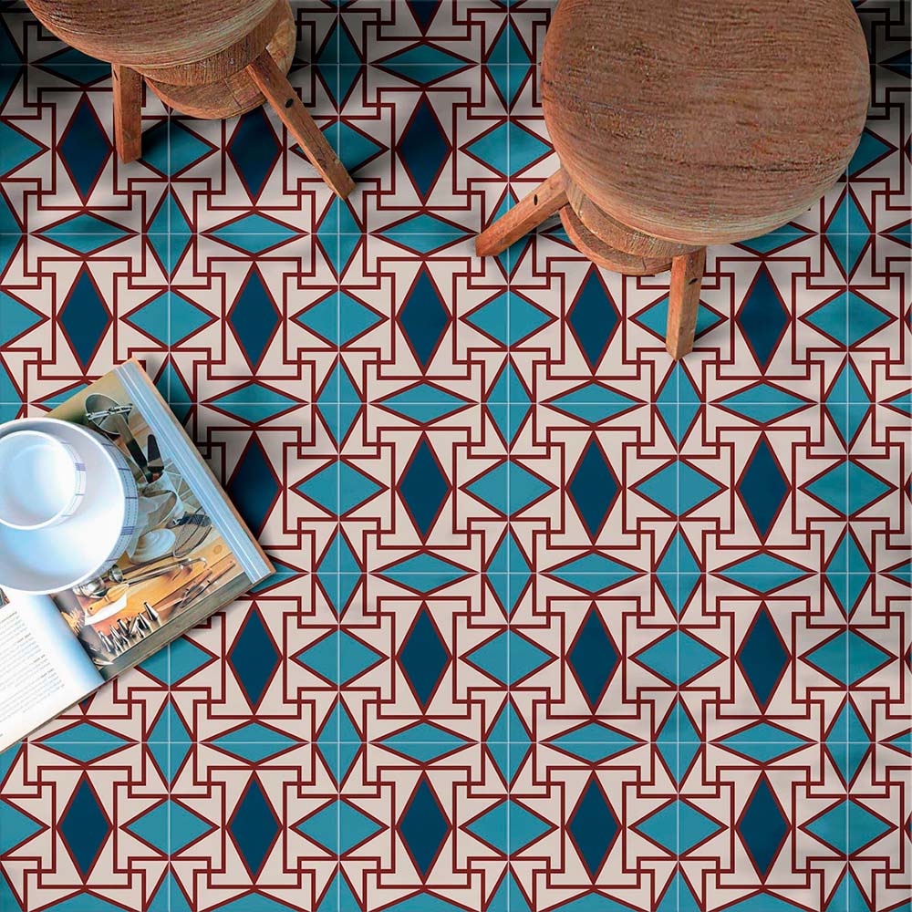 Interior floor styled with Abstract Iris Patterned Tiles in a 20x20cm format, featuring a striking geometric design in deep blue, teal and soft cream tones with fine red detailing. The repeating pattern creates a bold, decorative look, styled with wooden stools and accessories to showcase the tiles as a statement floor suitable for kitchens, dining spaces or feature areas.