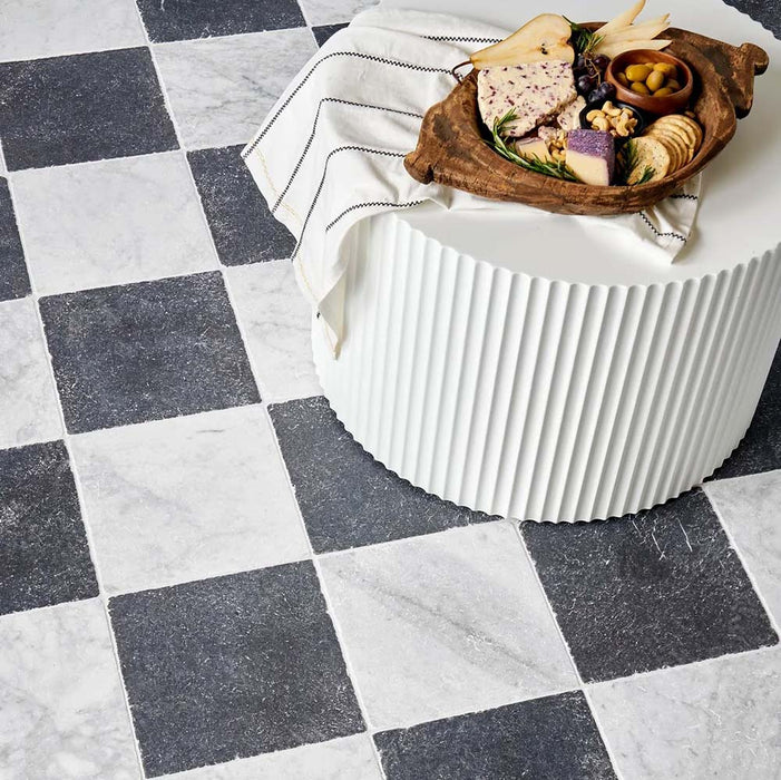 Interior setting featuring Fayrouz White 15.2x15.2cm natural marble tiles with a tumbled finish, installed in a classic chequerboard layout with black marble, styled with a fluted table and decorative serving board.