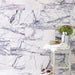 Bathroom interior featuring Fayrouz Lilac 30.5x61cm natural marble tiles with a honed finish, installed across walls and floor in a staggered layout, showcasing a soft white base with flowing lilac and grey veining, styled with a rustic wooden stool, brushed metal vase with greenery, and neutral accessories for a calm, refined space.