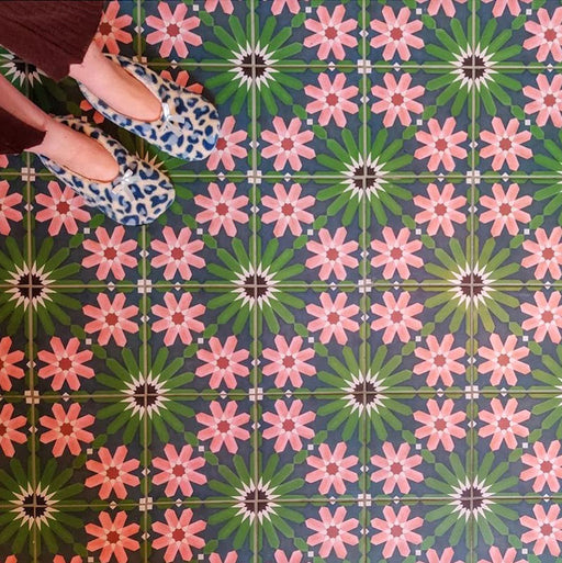 Floor featuring Fez Autumn 20x20cm Moroccan-style porcelain tiles, showcasing an intricate geometric floral pattern in deep green, navy and warm blush tones, styled with patterned slippers for a cosy, character-filled interior.