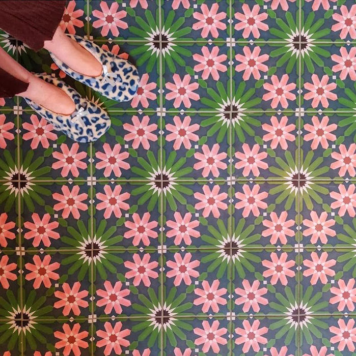 Floor featuring Fez Autumn 20x20cm Moroccan-style porcelain tiles, showcasing an intricate geometric floral pattern in deep green, navy and warm blush tones, styled with patterned slippers for a cosy, character-filled interior.