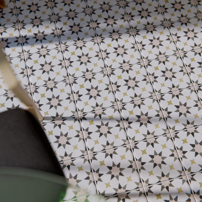 Marketing image of Agadir Natural Moroccan-style 20x20cm porcelain tiles laid on a floor, featuring a soft neutral geometric star pattern with subtle grey and warm beige tones, styled with a wooden chair for a lived-in look.