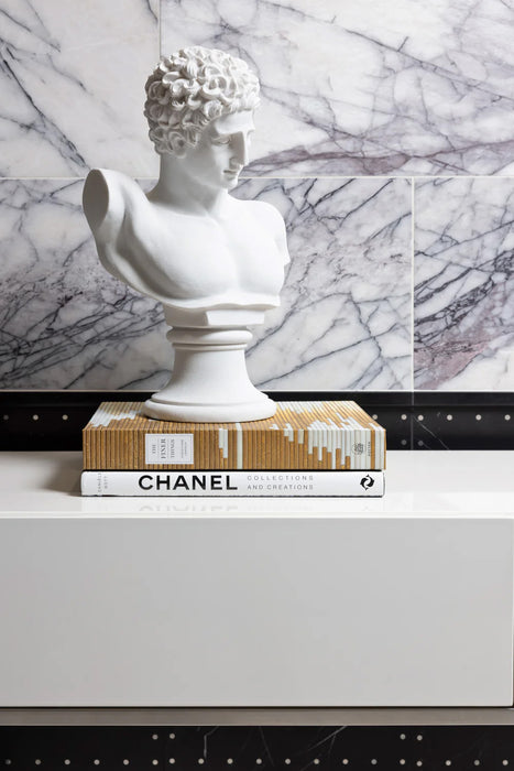 Interior detail featuring Fayrouz Lilac 30.5x61cm natural marble tiles with a honed finish, installed in a horizontal layout, showcasing a soft white base with elegant lilac and grey veining, styled with a classical sculpture and curated books to create a refined, gallery-inspired setting.
