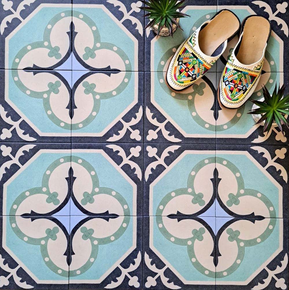 Flat-lay setting featuring London Streets Goodwin Court 20x20cm Victorian Moroccan style floor tiles, showcasing a soft blue, cream and charcoal geometric pattern, styled with decorative slippers and small plants for a lifestyle tile display.