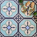 Flat-lay setting featuring London Streets Goodwin Court 20x20cm Victorian Moroccan style floor tiles, showcasing a soft blue, cream and charcoal geometric pattern, styled with decorative slippers and small plants for a lifestyle tile display.