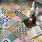 Fayrouz Mini Patchwork 15×15cm Moroccan-style porcelain tiles laid in a vibrant patchwork design, featuring an eclectic mix of geometric and floral motifs in soft pinks, sage green, deep blue, mustard yellow, terracotta and neutral tones, styled with decorative accessories for a warm, characterful interior look.
