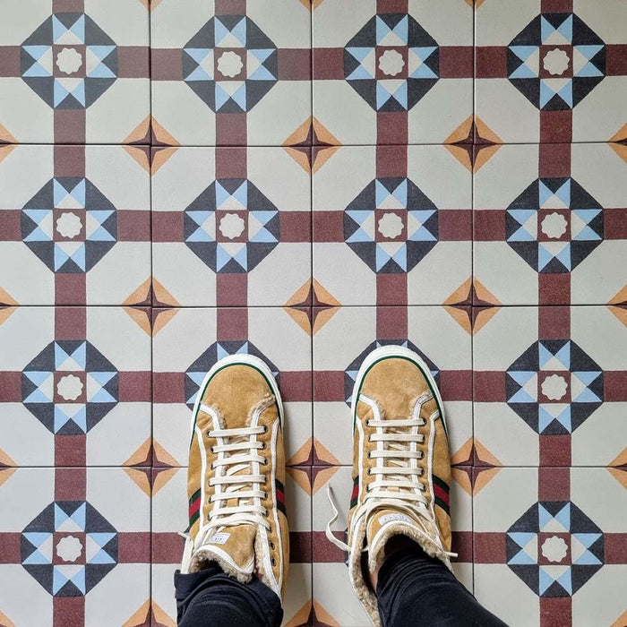 Flat-lay setting featuring London Streets Berlin Street 20x20cm Victorian Moroccan style floor tiles, showcasing the repeating geometric star pattern in burgundy, soft blue and cream tones, styled with trainers for a lifestyle tile display.