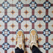 Flat-lay setting featuring London Streets Berlin Street 20x20cm Victorian Moroccan style floor tiles, showcasing the repeating geometric star pattern in burgundy, soft blue and cream tones, styled with trainers for a lifestyle tile display.