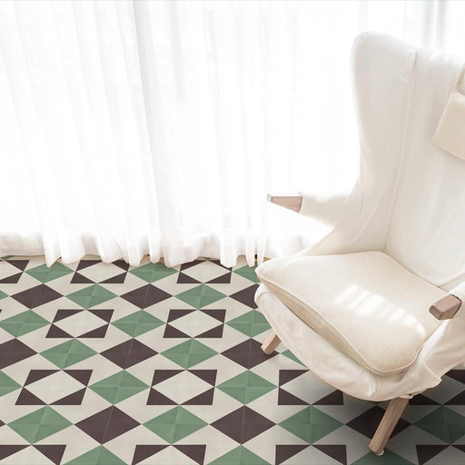 Living room interior featuring Abstract Angles Patterned Tiles in a 20x20cm format, laid as a geometric floor design. The repeating angular pattern in muted green, deep charcoal and soft cream tones creates a clean, contemporary look, styled with a white armchair and sheer curtains for a light, modern setting.
