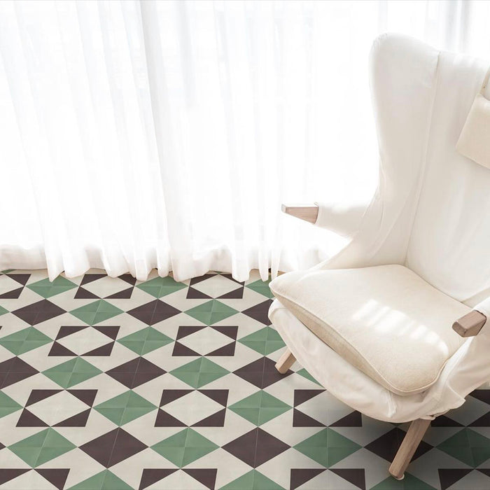 Living room interior featuring Abstract Angles Patterned Tiles in a 20x20cm format, laid as a geometric floor design. The repeating angular pattern in muted green, deep charcoal and soft cream tones creates a clean, contemporary look, styled with a white armchair and sheer curtains for a light, modern setting.