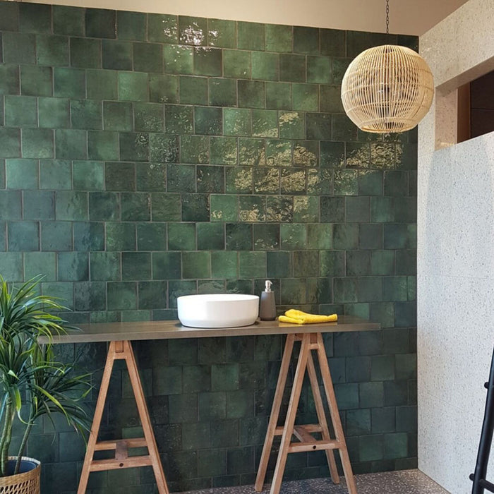 Interior feature wall showcasing Zellige Royal Green Square 13.2 × 13.2cm Moroccan-style ceramic tiles in rich deep green tones, laid in a neat grid behind a countertop basin, styled with timber trestles, natural textures and soft lighting for a bold, handcrafted zellige-effect look.