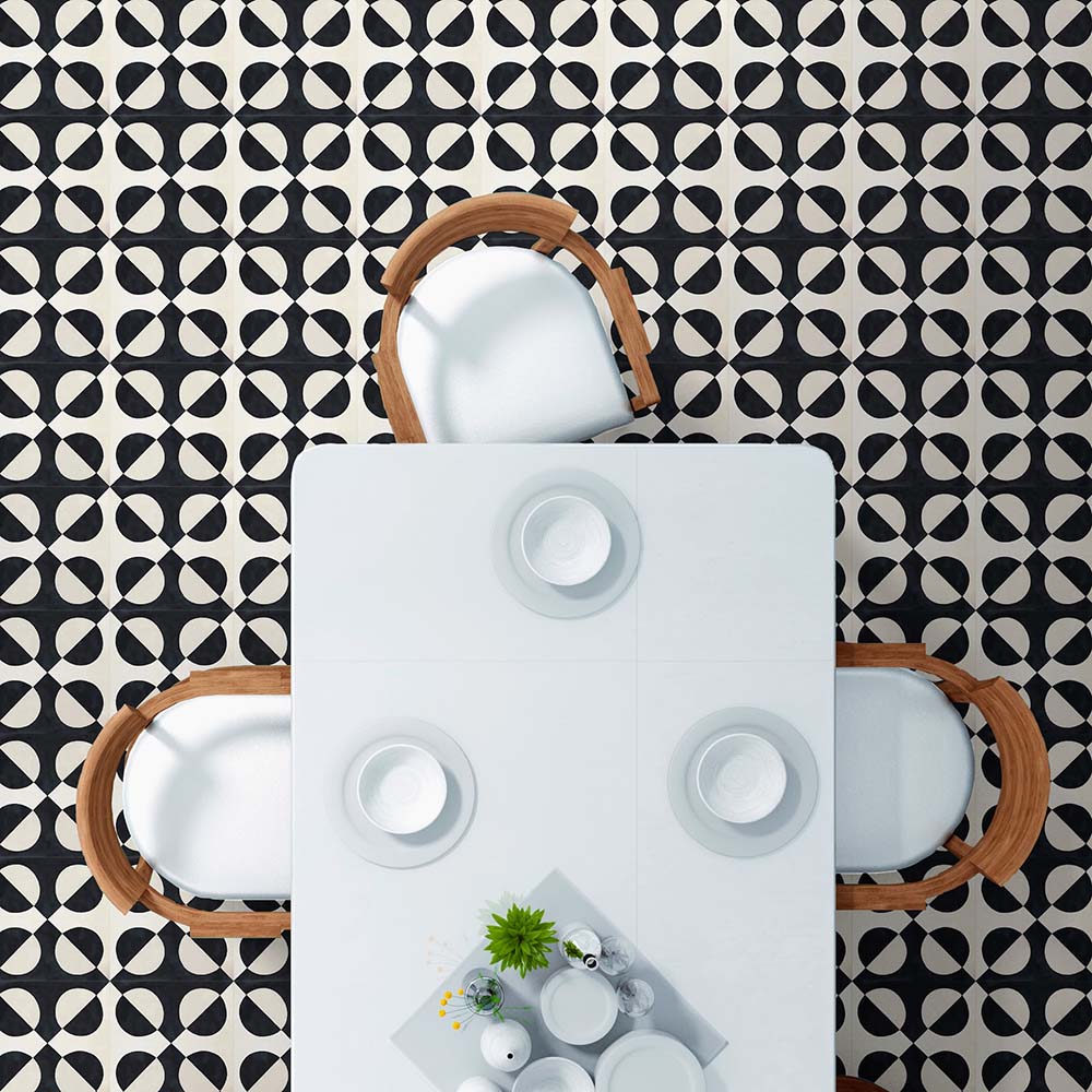Dining area styled with Abstract Illusion Noir Patterned Tiles in a 20x20cm format, laid as a bold geometric floor design. The high-contrast black and soft cream circular pattern creates a striking optical illusion effect, paired with a white dining table and wooden chairs for a clean, modern interior setting.