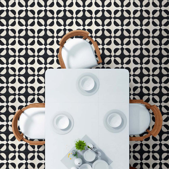 Dining area styled with Abstract Illusion Noir Patterned Tiles in a 20x20cm format, laid as a bold geometric floor design. The high-contrast black and soft cream circular pattern creates a striking optical illusion effect, paired with a white dining table and wooden chairs for a clean, modern interior setting.