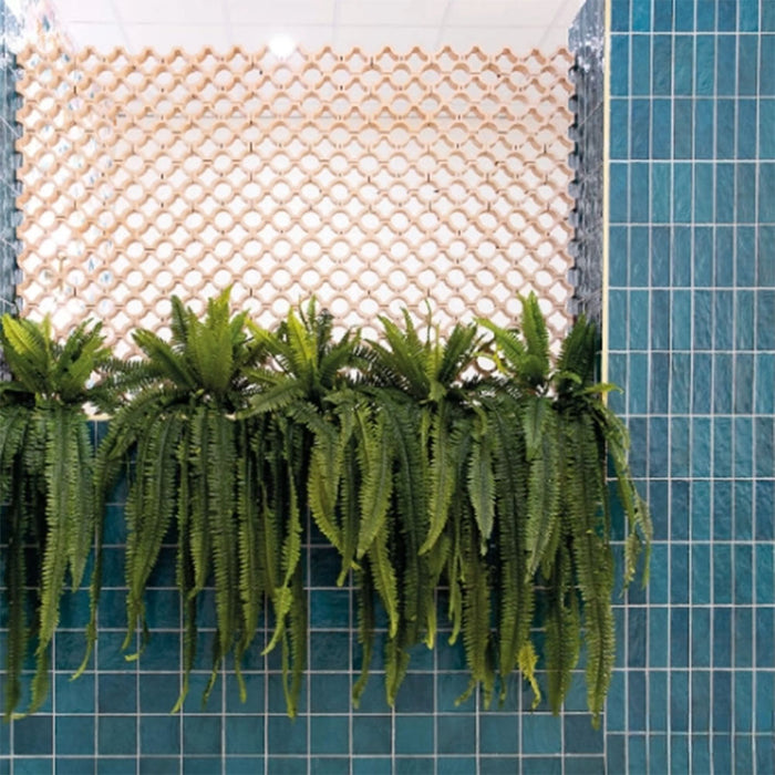 Interior wall featuring Zellige Peacock Green 6.5×20cm Moroccan-style ceramic brick tiles, showcasing rich blue-green tones and a glossy handmade-look finish, styled with trailing plants and a decorative patterned screen for a bold, contemporary feel.