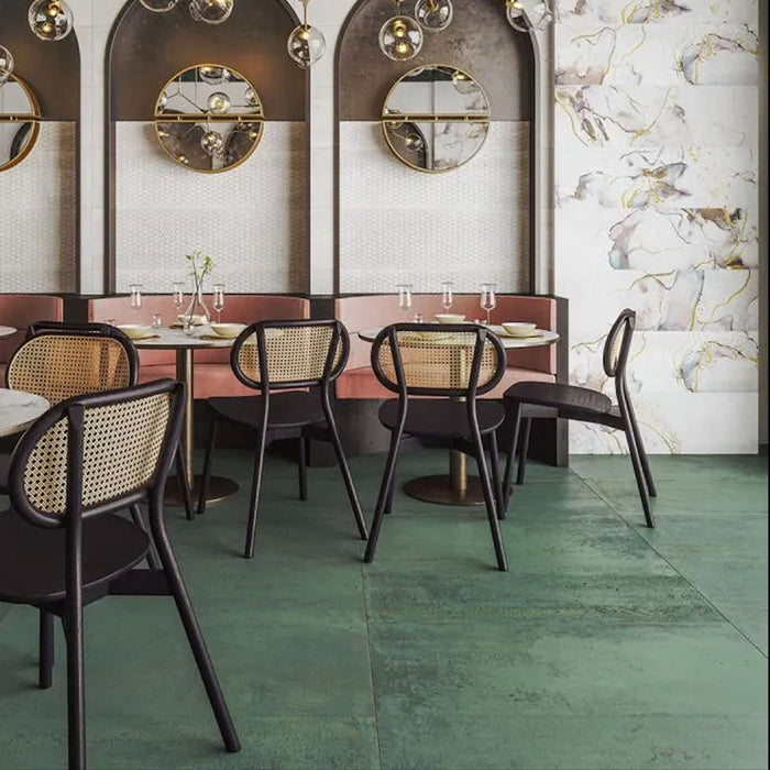 Contemporary restaurant interior featuring Mediterraneo Green 2cm outdoor slabs 50 × 100cm, showcasing deep green stone-effect porcelain tiles, paired with cane dining chairs, brass lighting, and floral marble-effect feature walls.