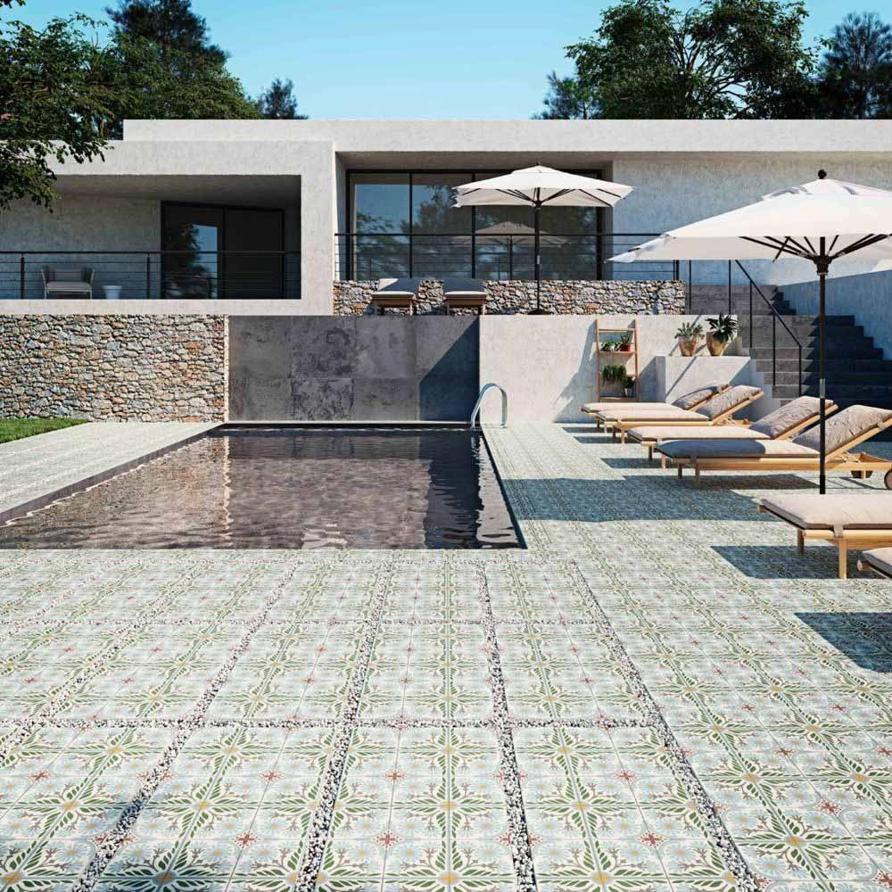 Modern outdoor pool area featuring Mediterraneo Olbia 2cm patterned outdoor slabs 50 × 100cm, showcasing a faded Mediterranean-inspired design in soft green and neutral tones, paired with sun loungers and contemporary architecture.