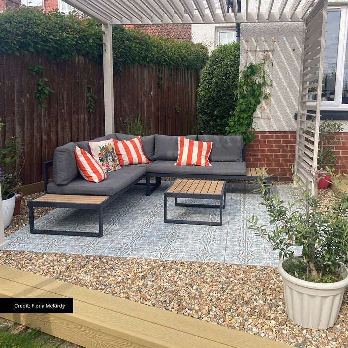 Outdoor seating area featuring Mediterraneo Olbia 2cm Patterned Outdoor Slabs 50x100cm, showcasing a decorative Mediterranean-style pattern in soft blue, green and terracotta tones, paired with contemporary garden furniture, gravel borders and a pergola-covered terrace.