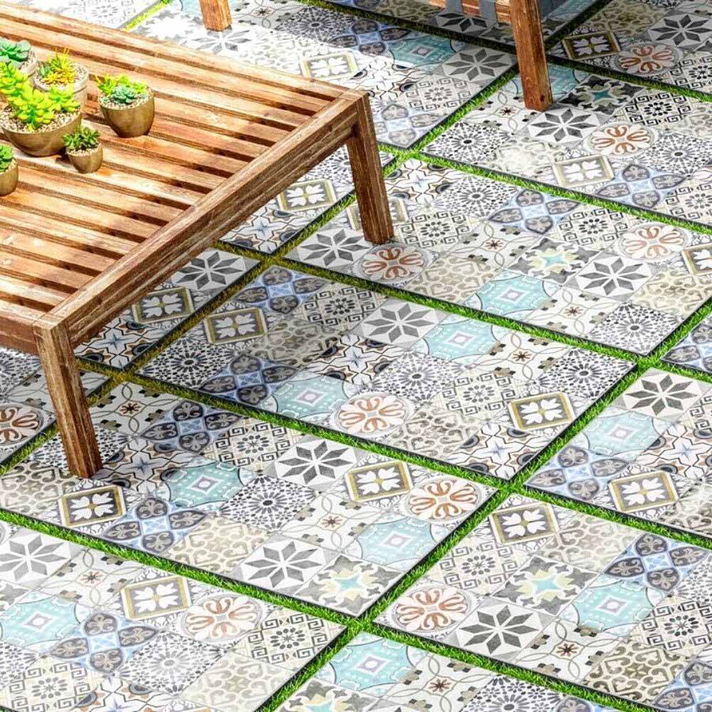 Outdoor seating area featuring Mediterraneo Patchwork 2cm patterned outdoor slabs 50 × 100cm, showcasing a mixed patchwork-inspired design in soft blue, grey, beige, and cream tones, paired with natural wood garden furniture.